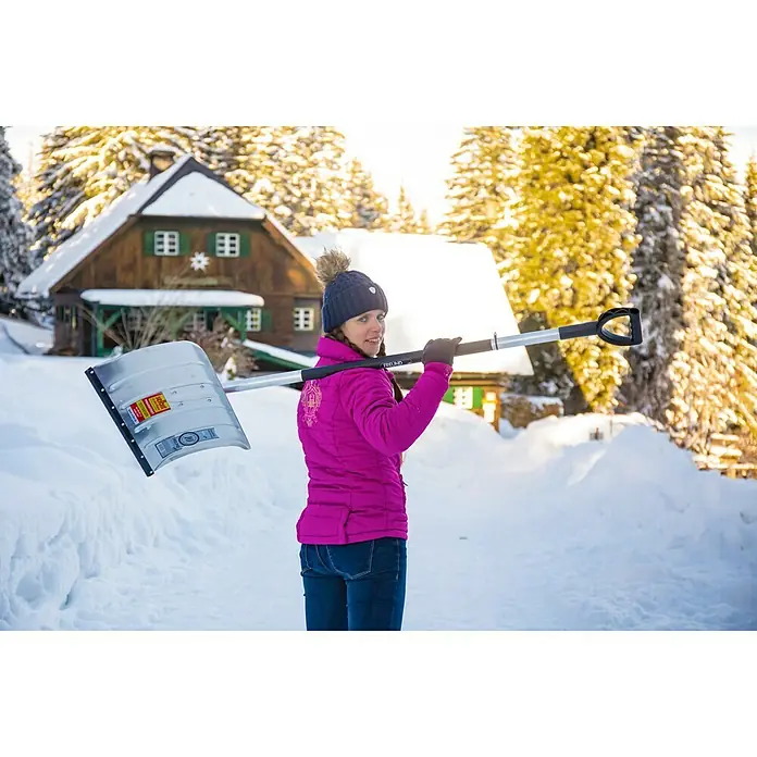 Freund Victoria Aluline Schneeschieber - Breite: 50 cm, Langstiel - Frau mit FREUND Winter Schneeschaufel vor einem eingeschneiten Haus.