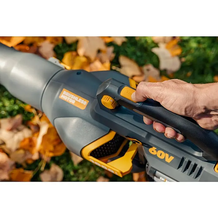 Worx ENVIRO Akku-Laubbläser EG560.9 - 60 V, Ohne Akku, Blasgeschwindigkeit: 200 km/h, Blasleistung: 1.000 m³/h - Detailaufnahme eines 60V-Akkubläsers mit bürstenlosem Motor, der von einer Hand bedient wird, vor einem Hintergrund aus Herbstlaub.