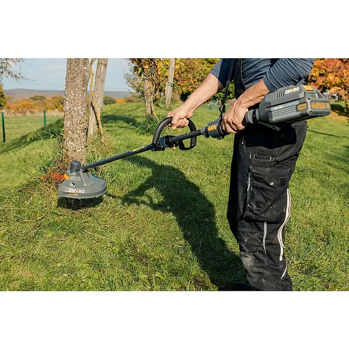 Worx ENVIRO Akku-Rasentrimmer EG161.9 - 60 V, Ohne Akku - Ein Mann, der einen ENVIRO 60V Akku-Rasentrimmer benutzt, um Gras um einen Baum herum zu trimmen.