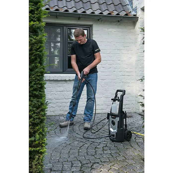 PowerPlus Hidrolimpiadora de alta presión POWXG90405 - 110 bar, 1.400 W, Capacidad de bombeo: 390 l/h - Un hombre usa una hidrolimpiadora Powerplus para limpiar una zona exterior pavimentada. El dispositivo está de pie junto a él, con un cable amarillo.