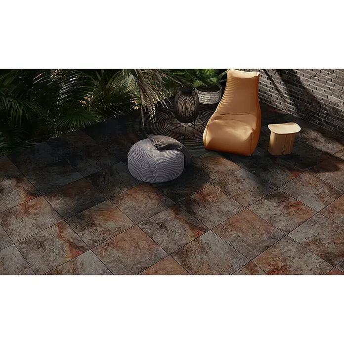 Pavimento porcelánico Vulcan - 60,8 x 60,8 cm, Magma, Mate - Un espacio al aire libre con suelo de baldosas, un puf, una mesa auxiliar y una exuberante vegetación, creando un ambiente acogedor y elegante.