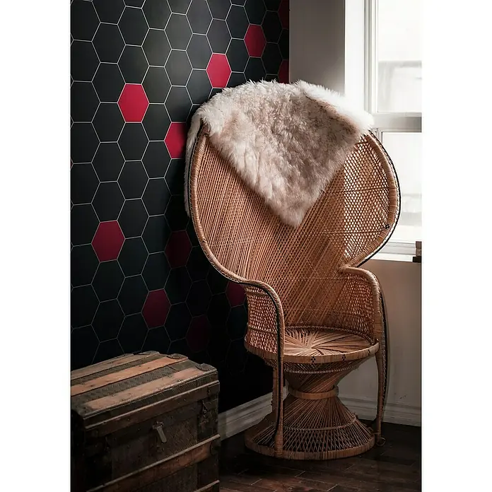 Selbstklebemosaik Hexagon Uni SAMT CHA1R - 15,2 x 17,2 cm, Rot, Matt - Ein dekorativer Innenraum mit einem eleganten Korbsessel mit weichem Fellbezug, der vor einer stilvollen Wand mit Sechseckmuster steht.