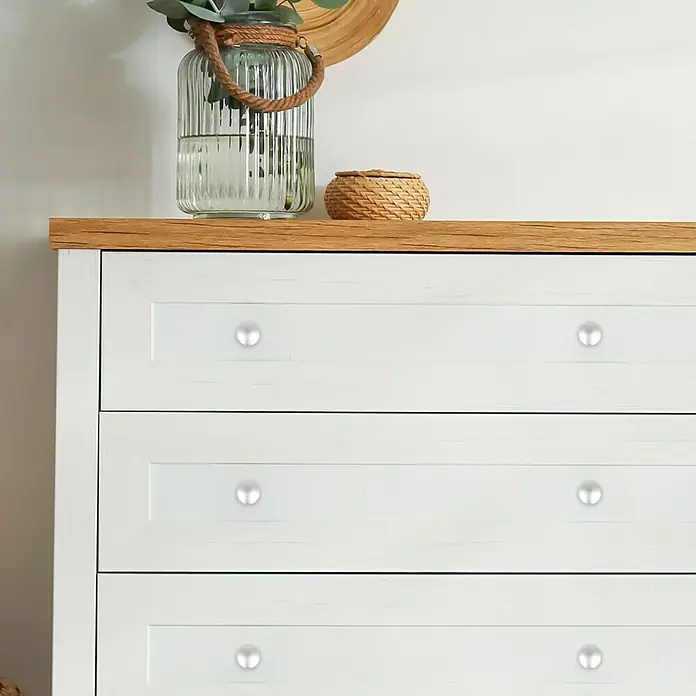 Häfele Pomo para muebles - Tipo de tirador del mueble: Botón, Ø x Al: 25 x 22 mm, Niquelado - Cómoda blanca con tapa de madera, decorada con un jarrón de cristal y una cesta. Los cajones están acabados con pomos plateados.