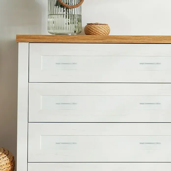 Häfele Tirador para muebles - Cromado, Distancia entre orificios: 128 mm - Un primer plano de una cómoda blanca con una tapa de madera y tiradores plateados. Elementos decorativos colocados en él.