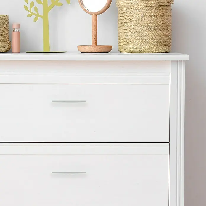 Rei Tirador para muebles - Distancia entre orificios: 96 mm, Tipo de tirador del mueble: Barra, Aluminio - Primer plano de una cómoda blanca con dos cajones y tiradores plateados, con objetos decorativos encima.