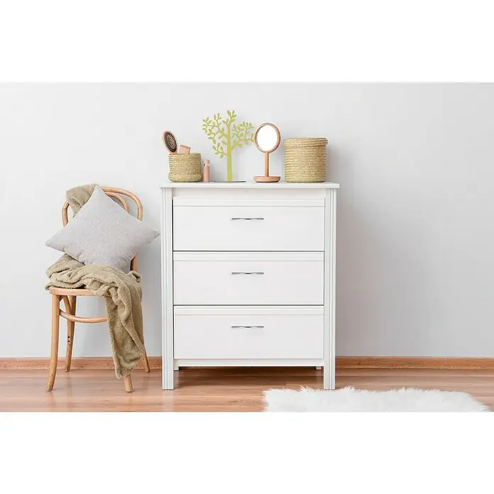 Häfele Tirador para muebles - L x An x Al: 158 x 11 x 29 mm, Tipo de tirador del mueble: Estribo, Distancia entre orificios: 128 mm, Otros, Cromado, Brillante - Cómoda blanca con tres cajones, adornada con cestas y un espejo, junto a una silla con cojín y manta.