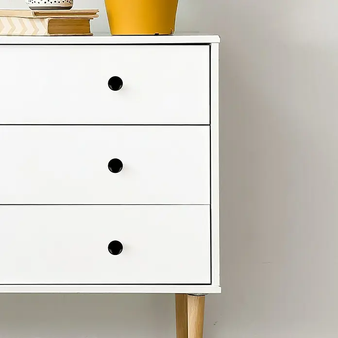 Rei Pomo para muebles - Tipo de tirador del mueble: Botón, Ø x Al: 33 x 27 mm, Negro - Primer plano de una cómoda blanca con tres cajones y pomos negros, decorada con una planta y libros.