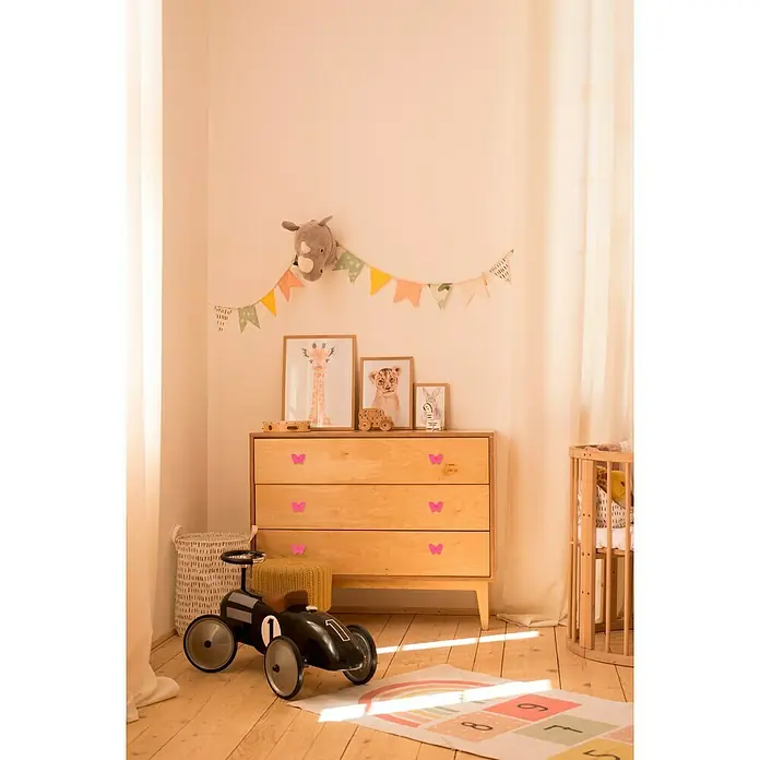 Häfele Pomo infantil para mueble - Botón, Ø x Al: 70 x 53 mm, Lila, Mariposa - La habitación de los niños presenta una cómoda de madera con mariposas, decoraciones y un coche de juguete, creando un ambiente acogedor y lúdico.