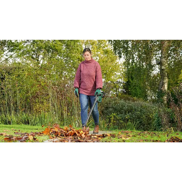Bosch Power for All 18V Akku-Laubbläser UniversalLeafBlower 18V-130 - 18 V, Li-Ionen, Ohne Akku, Blasgeschwindigkeit: 185 km/h - Eine Frau benutzt einen Laubbläser, um Herbstlaub auf einem Rasen zu entfernen. Laubbläser von Bosch für eine mühelose Gartenarbeit im Herbst.