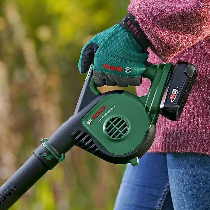 Bosch Power for All 18V Akku-Laubbläser UniversalLeafBlower 18V-130 - 18 V, Li-Ionen, Ohne Akku, Blasgeschwindigkeit: 185 km/h - Eine Person hält einen grünen Bosch Laubbläser mit Akku und Handschuhen.