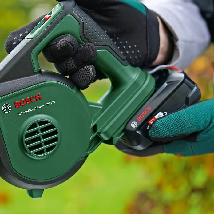 Bosch Power for All 18V Akku-Laubbläser UniversalLeafBlower 18V-130 - 18 V, Li-Ionen, Ohne Akku, Blasgeschwindigkeit: 185 km/h - Nahaufnahme eines Bosch UniversalLeafBlower 18V-130 Laubbläsers, der von einer Person mit Gartenhandschuhen gehalten wird.