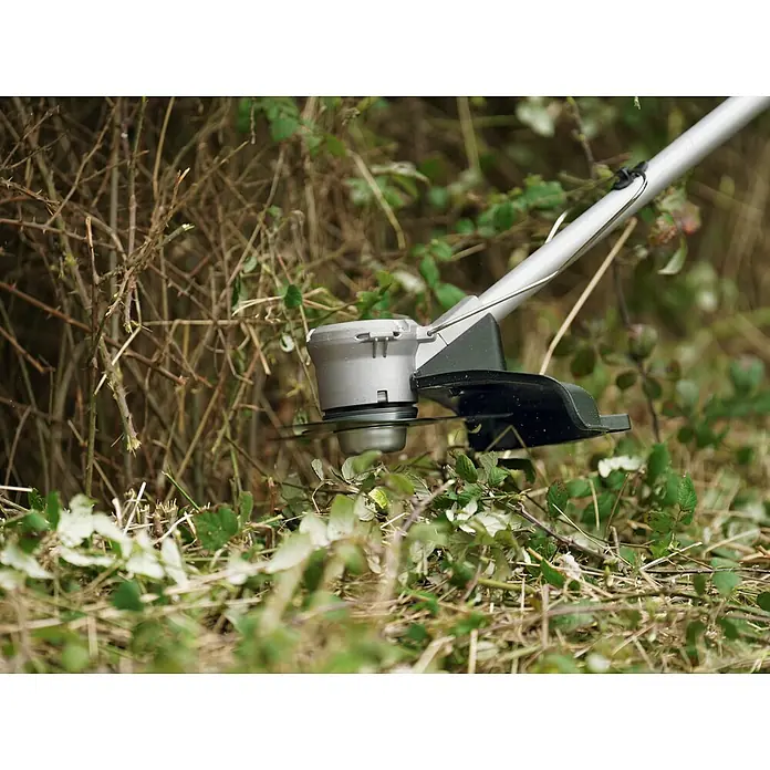 Bosch Power for All 36V Akku-Rasentrimmer AdvancedBrushCut 36V-23-750 - 36 V, 2 Ah, Li-Ionen, 1 Akku, Schnittbreite Messer: 23 cm, Schnittbreite Faden: 33 cm - Nahaufnahme eines Rasentrimmers, der durch dichtes Gras und Büsche schneidet. Das Gerät ist silbern mit schwarzen Akzenten und gut sichtbar.