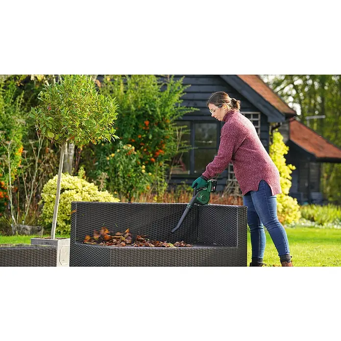 Bosch Power for All 18V Akku-Laubbläser UniversalLeafBlower 18V-130 - 18 V, Li-Ionen, Ohne Akku, Blasgeschwindigkeit: 185 km/h - Frau reinigt Gartenmöbel mit einem Laubbläser, um die herabgefallenen Blätter zu entfernen. Das Gerät ist kabellos und einfach zu bedienen.