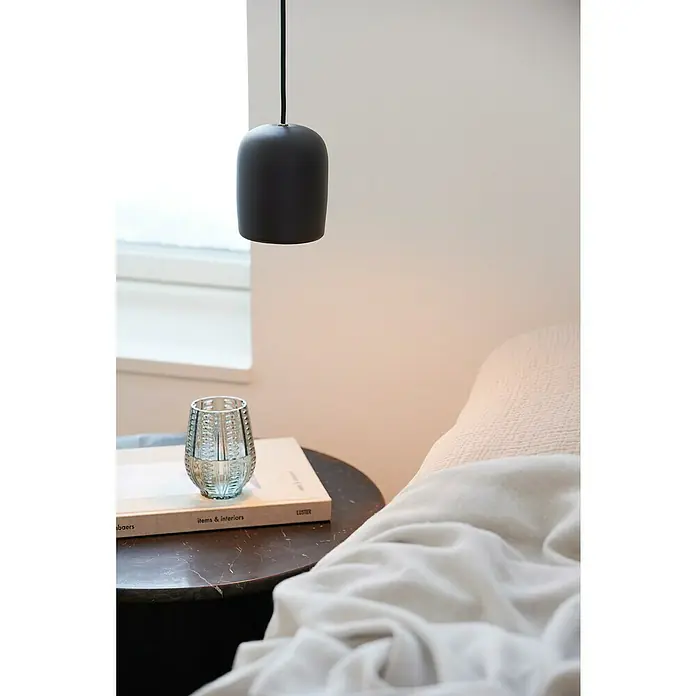 Nordlux Notti Lámpara colgante redonda - 25 W, Ø x Al: 10 x 12 cm, Negro, Negro, E27 - Una elegante lámpara colgante de material oscuro cuelga sobre una mesa de noche con un libro y un vaso. Interior minimalista.