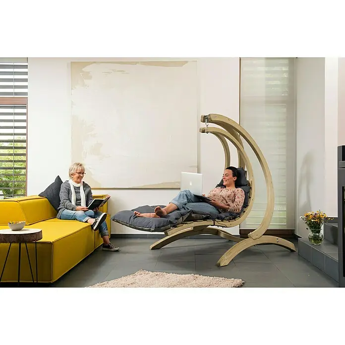 Amazonas Hängeliege Swing Lounger - L x B x H: 240 x 75 x 114 cm, Anthrazit - Wohnzimmer mit einem gelben Sofa und einem schwebenden Liegestuhl mit Holzrahmen, auf dem eine Frau mit Laptop liegt.