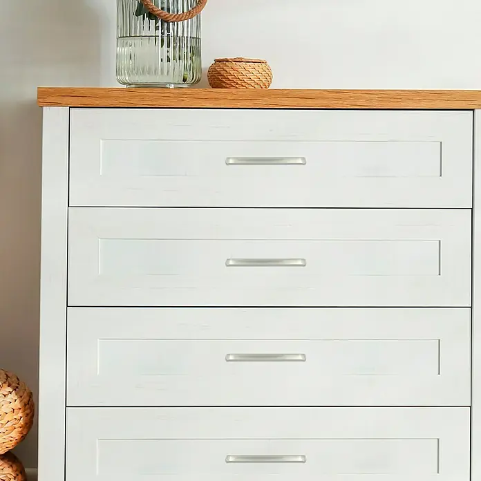 MöbelgriffTyp Möbelgriff: Bügel, B x L: 30 x 160 mm - Eine weiße Kommode mit vier Schubladen und silbernen Griffen unter einem Holzregal, auf dem sich ein dekoratives Glas und Korb befinden.