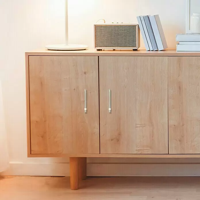 Häfele Tirador para muebles - Tipo de tirador del mueble: Barra, Distancia entre orificios: 96 mm - Un mueble de madera clara con tres puertas y elegantes tiradores metálicos, con libros y un altavoz en su superficie.