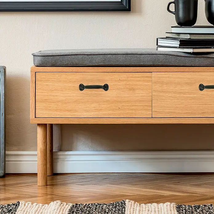 Häfele Tirador para muebles - Tipo de tirador del mueble: Estribo, Distancia entre orificios: 99 mm, Acero, Brillante, Negro - Primer plano de una cómoda de madera con tiradores negros y un cojín de asiento gris.