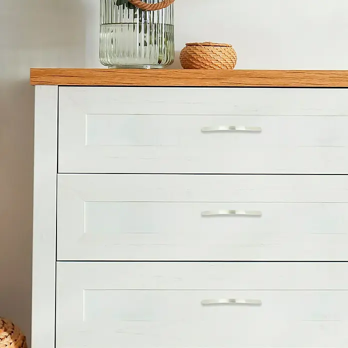 Häfele Tirador para muebles - L x An x Al: 149 x 10 x 31 mm, Distancia entre orificios: 128 mm - Primer plano de una cómoda blanca con tres cajones y tiradores plateados, que muestra un mueble elegante y práctico.