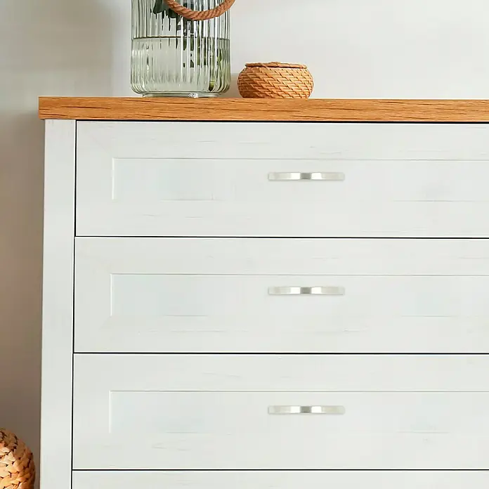 Häfele Möbelgriff - L x B x H: 112 x 10 x 31 mm, Lochabstand: 96 mm - Nahaufnahme einer weißen Kommode mit drei Schubladen und silbernen Griffen, die ein schlichtes und modernes Design aufweist.