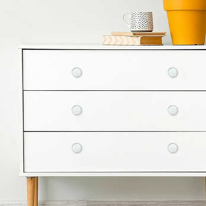 Häfele Pomo para muebles - Tipo de tirador del mueble: Botón, Plástico, Cromado, Blanco - Primer plano de una cómoda blanca con seis pomos redondos, con una taza y libros encima.