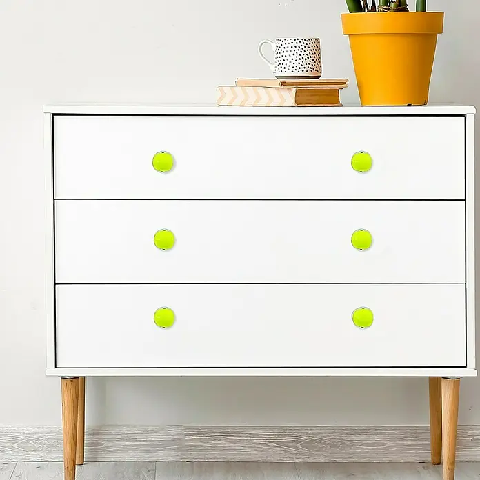 Häfele Pomo para muebles - Tipo de tirador del mueble: Botón, Plástico, Cromado, Verde - Un primer plano de una cómoda blanca con seis pomos amarillos brillantes que sirven como tiradores de cajones. Elementos decorativos están colocados en la parte superior.