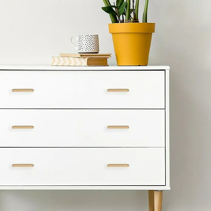 Häfele Tirador para muebles - Madera, Lacado, An x L: 30 x 100 mm, Haya - Cómoda con tres cajones y tiradores de madera, coronada con una maceta que contiene una planta verde y una taza.
