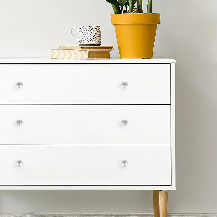 Häfele Pomo para muebles - Tipo de tirador del mueble: Botón, Ø x Al: 28 x 25 mm, Cromado, Mate - Una cómoda blanca con tres cajones y tiradores de cristal, con elementos decorativos como una taza, libros y una planta en maceta encima.