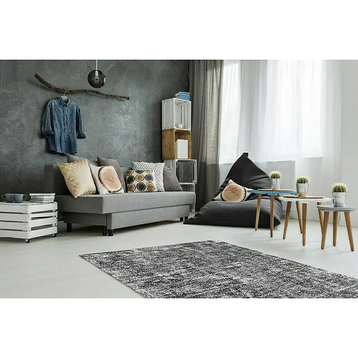 Kayoom Kurzflorteppich Etna - Anthrazit, 230 x 160 cm, 100 % Mikropolyester - Wohnzimmer-Szene mit einem stilvollen grauen Sofa, einem bequemen Sitzsack und einem gemusterten Teppich, der dem Raum Textur verleiht.