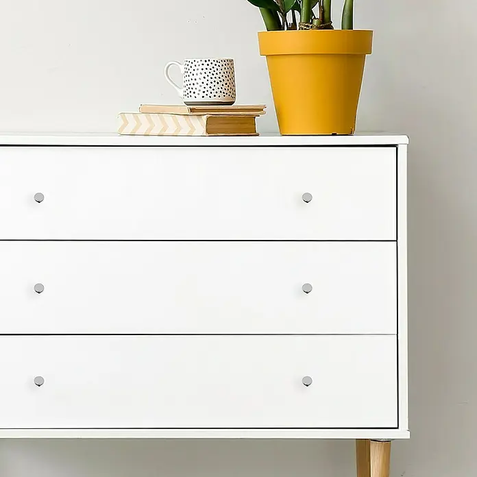 Häfele Pomo para muebles - Tipo de tirador del mueble: Botón, Ø x Al: 11 x 25 mm, Resplandeciente, Cromo - La imagen muestra una cómoda blanca con tres cajones, complementada con libros, una taza y una planta en maceta. Diseño limpio para espacios modernos.