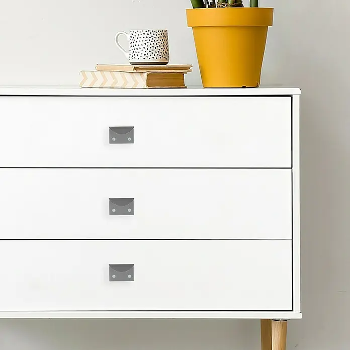 Häfele Tirador para muebles - L x An x Al: 34 x 50 x 38 mm - Cómoda blanca con tres cajones y tiradores grises. En la parte superior de la cómoda hay libros, una taza y una maceta con una planta.