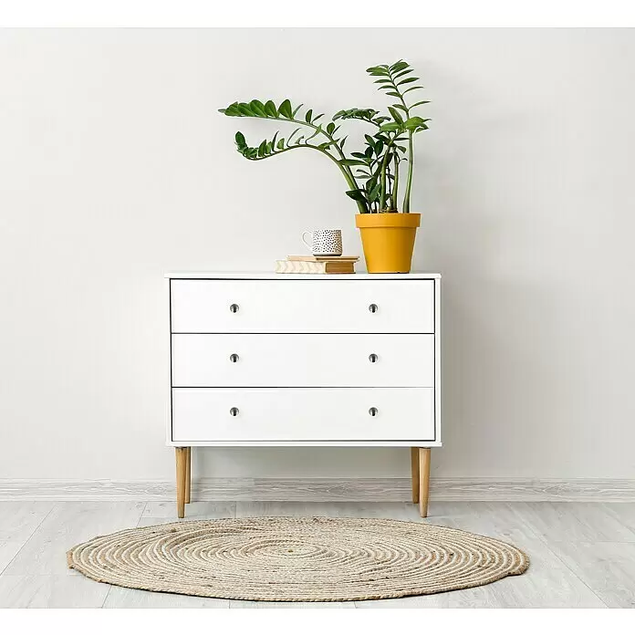 Häfele Pomo para muebles - Tipo de tirador del mueble: Botón, Ø x Al: 28 x 25 mm - Cómoda blanca de 3 cajones con patas de madera clara, pomos metálicos, decorada con una planta y libros, sobre un suelo claro con una alfombra redonda.