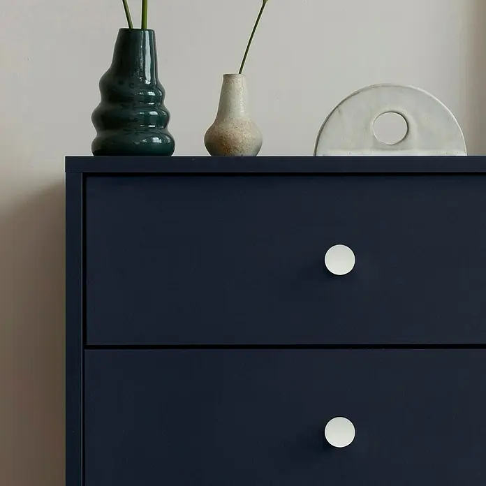 Häfele Pomo para muebles - Tipo de tirador del mueble: Botón, Ø x Al: 26 x 27 mm, Plástico - Cómoda azul oscuro con dos cajones y pomos redondos claros. Jarrones decorativos y una escultura se encuentran en la superficie.
