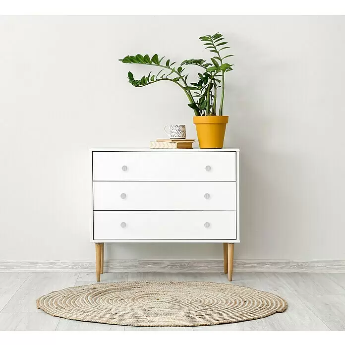 Häfele Pomo para muebles - Tipo de tirador del mueble: Botón, Ø x Al: 25 x 27 mm, Brillante - Cómoda blanca con patas de madera clara. Encima hay una planta, una taza y libros, y en el suelo una alfombra redonda de yute.