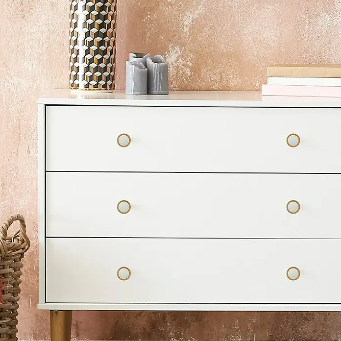 Häfele Pomo para muebles - Tipo de tirador del mueble: Botón, Ø x Al: 50 x 19,5 mm, Lacado, Blanco, Roble - Primer plano de una cómoda blanca con seis pomos dorados sobre una pared rosa.