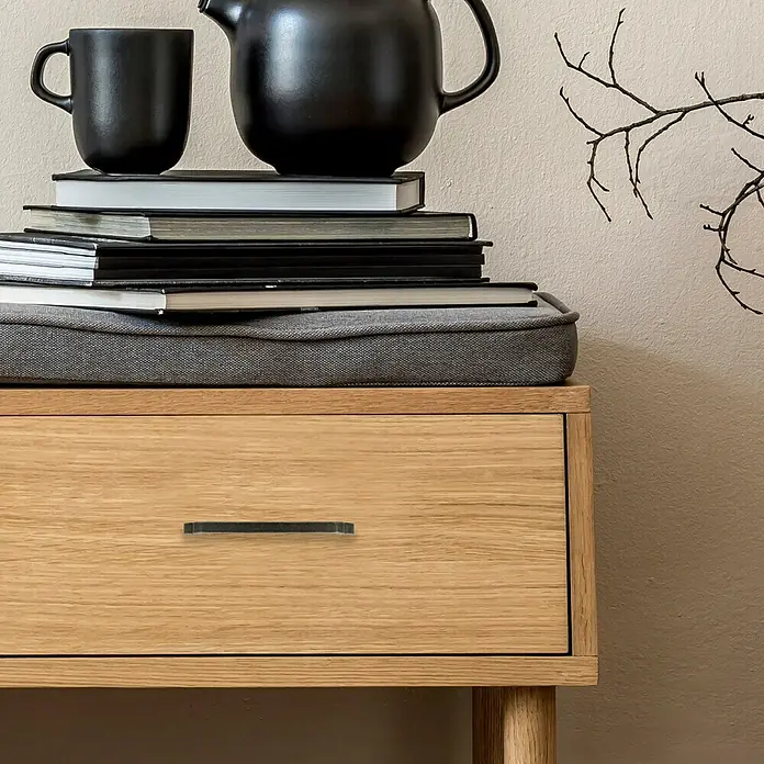 Häfele Tirador para muebles - Tipo de tirador del mueble: Estribo, L x An x Al: 180 x 30 x 12 mm - Primer plano de una cómoda con una taza y una tetera sobre libros, que muestra una solución de almacenamiento elegante y funcional.