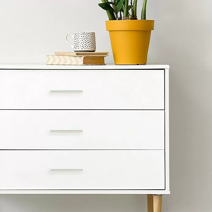 Häfele Tirador para muebles - Tipo de tirador del mueble: Estribo, L x An x Al: 219 x 32 x 20 mm, Aluminio, Lacado, Blanco - Cómoda blanca con tres cajones anchos y tiradores discretos, con una planta, libros y una taza encima.