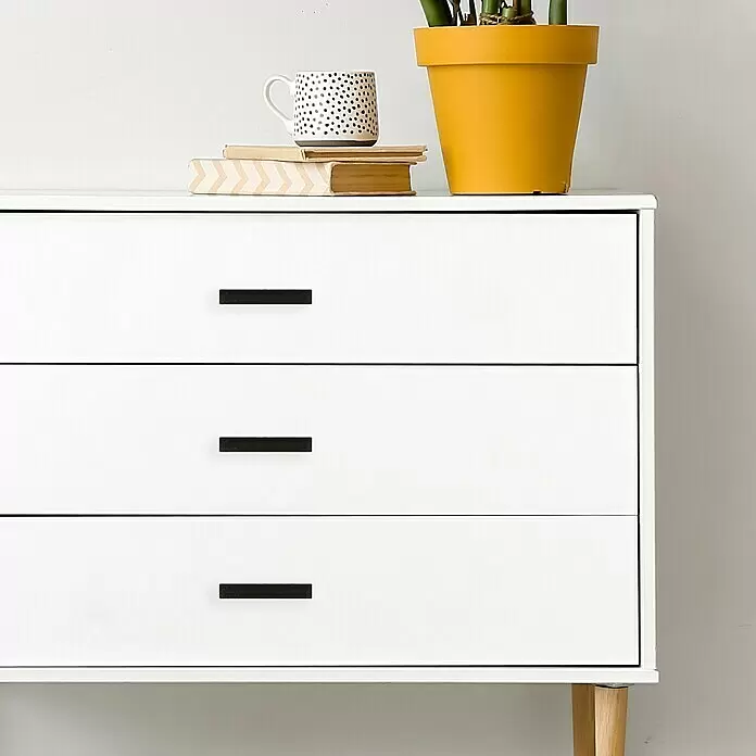 Häfele Tirador para muebles - Tipo de tirador del mueble: Estribo, L x An x Al: 154 x 26 x 25 mm - Una cómoda blanca con tres cajones, cada uno con un tirador rectangular negro. Encima hay una planta y libros.