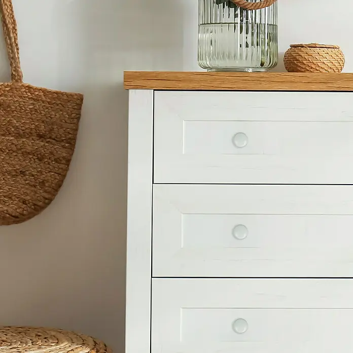 Häfele Pomo para muebles - Tipo de tirador del mueble: Botón, Ø x Al: 37 x 21 mm, Porcelana - Primer plano de una cómoda blanca con tres cajones y tablero de madera, decorada con un jarrón y una cesta.