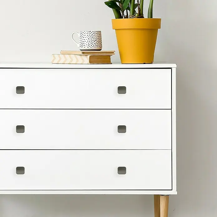 Häfele Tirador para muebles - Tipo de tirador del mueble: Barra, L x An x Al: 44 x 40 x 25,5 mm, Aluminio, Niquelado - Una moderna cómoda blanca con tres cajones y tiradores cuadrados minimalistas, decorada con una planta y una taza.