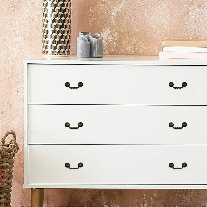 Häfele Tirador para muebles - Tipo de tirador del mueble: Estribo, L x An x Al: 88 x 17 x 33 mm - Primer plano de una cómoda blanca con tres cajones, complementada con elementos decorativos como un jarrón y velas encima.