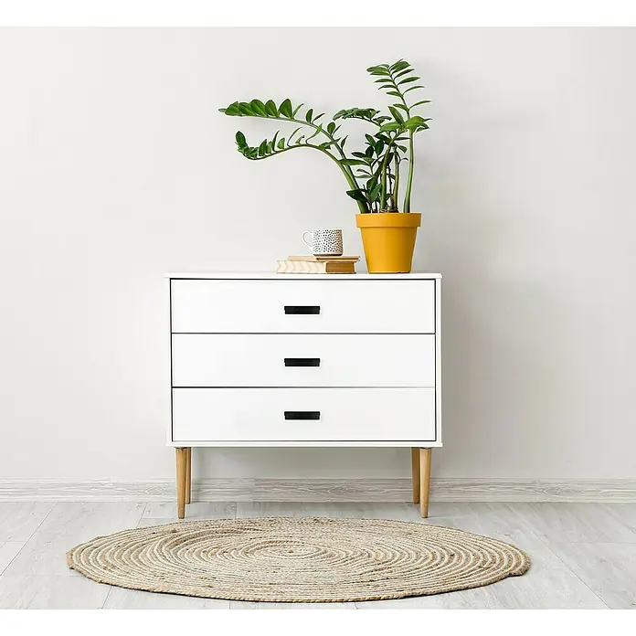 Häfele Tirador para muebles - Tipo de tirador del mueble: Concha, L x An x Al: 170 x 21 x 40 mm, Negro - Elegante cómoda blanca con tres cajones, decorada con una planta en maceta y una taza, sobre una alfombra redonda.