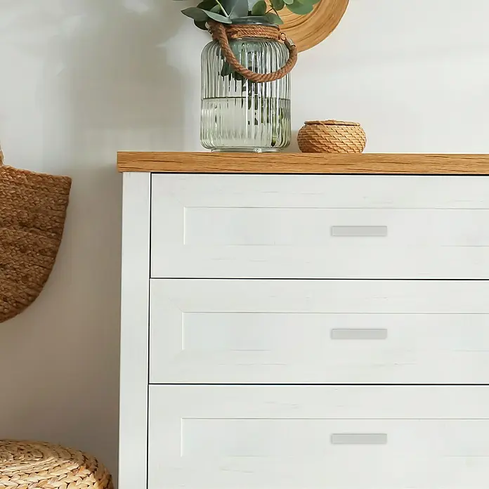 Häfele MöbelgriffTyp Möbelgriff: Stange, L x B x H: 80 x 14 x 13 mm, Aluminium, Sonstige - Kommode aus Holz und weißen Schubladen mit silbernen Griffen, mit Glasvase und dekorativem Korb. Ideal für Schlafzimmer und Wohnbereich.