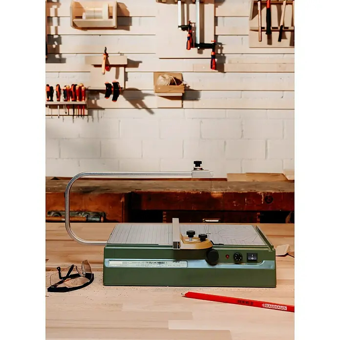 Proxxon Micromot Heißdraht-Schneidegerät Thermocut 230/E - 1 x Heißdraht-Schneidegerät Thermocut 230/E, 1 x Sattel und Drahtspule (30 m Schneidedraht Ø 0,2 mm) - Die Dekupiersäge von Proxxon mit Schutzbrille und Bleistift auf einer Werkbank.