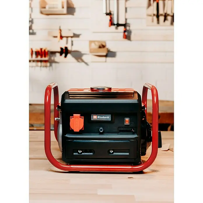 Einhell Stromerzeuger TC-PG 10/E5 - Nennleistung: 680 W, Tankvolumen: 4 l - Nahaufnahme eines Einhell Stromerzeugers mit rotem Rahmen, der auf einem Holztisch steht. Werkzeuge sind an der Wand im Hintergrund befestigt.