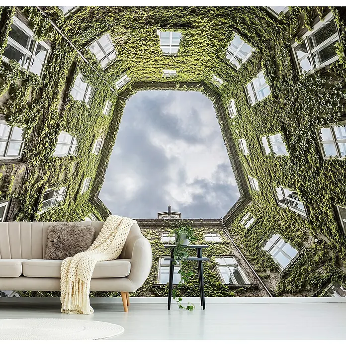 Papermoon Premium collection Fototapete Wiener Hof - B x H: 200 x 149 cm, Vlies - Ein Innenraum mit einer Couch und einem Tisch vor einer Tapete mit einem Gebäudehof, der mit Efeu bedeckt ist.