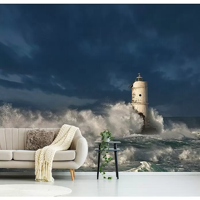 Papermoon Premium collection Fototapete Faro di Mangiabarche - B x H: 450 x 280 cm, Vlies - Wandbild mit stürmischer Leuchtturmszene und tosenden Wellen, hinter einem Sofa in einem modernen Wohnzimmer angebracht.