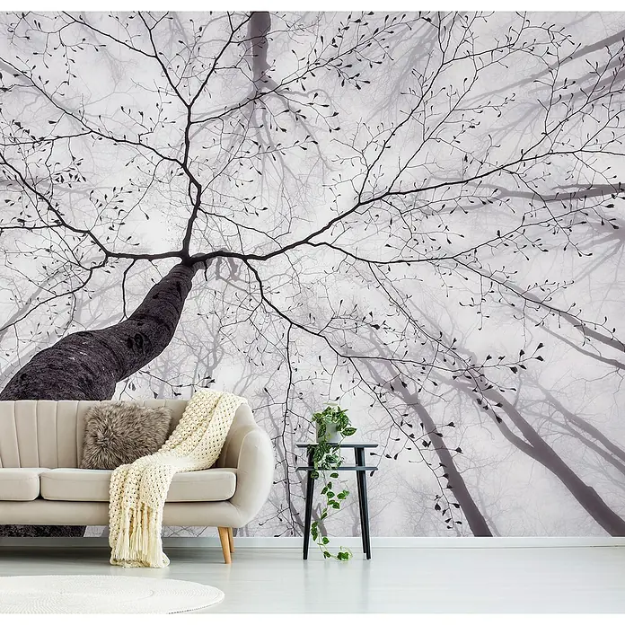 Papermoon Premium collection Fototapete Waldblick nach oben - B x H: 250 x 186 cm, Vlies - Wohnzimmer mit beigem Sofa, Kissen und Decke vor einer Baumtapete, die eine ruhige und stilvolle Atmosphäre schafft.