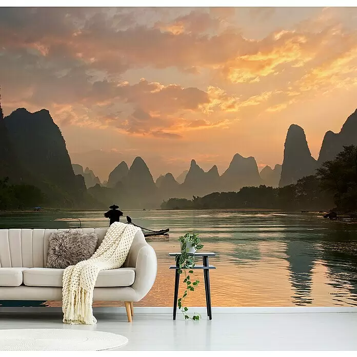 Papermoon Premium collection Fototapete Golden Li River - B x H: 450 x 280 cm, Vlies - Eine gemütliche Wohnzimmereinrichtung mit beigem Sofa, flauschigem Kissen und Strickdecke, neben einem schwarzen Beistelltisch mit Pflanze, vor einem Wandbild.