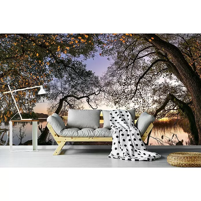 Papermoon Premium collection Fototapete Herbst am See - B x H: 500 x 280 cm, Vlies - Holz-Tagesbett mit grauen Kissen und gepunkteter Decke in einem Raum mit Natur-Wandbild. Daneben stehen eine Lampe und ein kleiner Tisch.